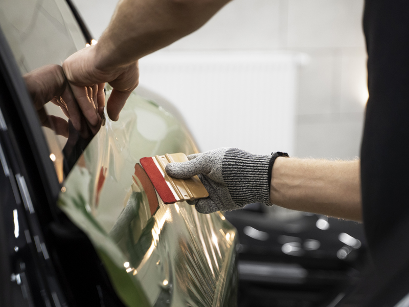 Installer applying clear paint protection film to a car panel