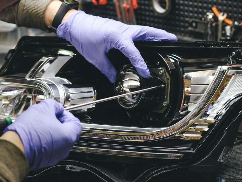 Technician fitting a projector lens into a car headlight