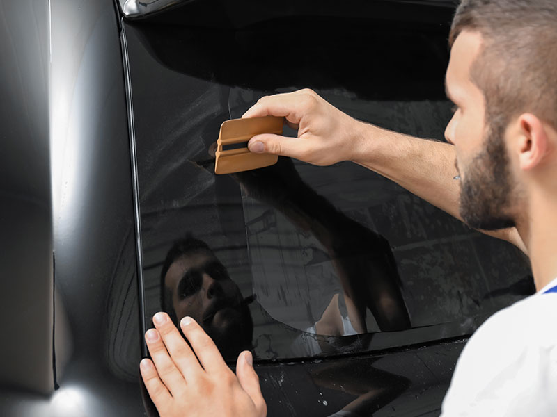 Installer squeegeeing window tint film onto a black car door