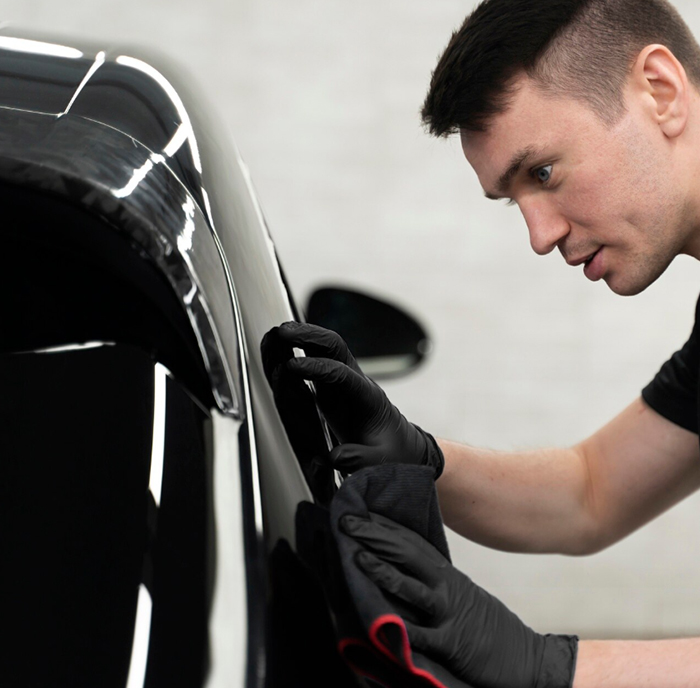 Technician applying protective film to a black car
